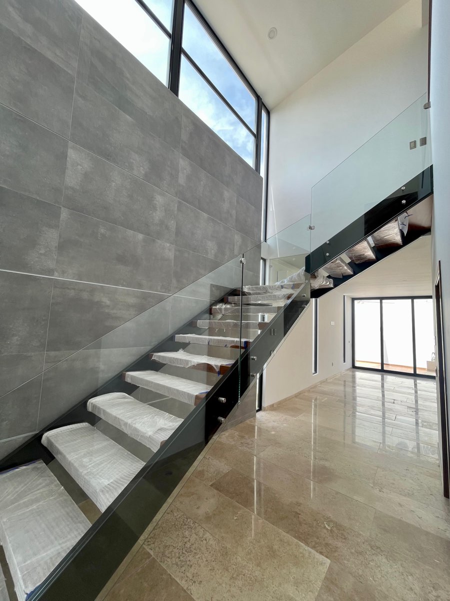Escalera de doble altura con barandal de cristal y piso de mármol en casa de Paraíso Marina, Mazatlán