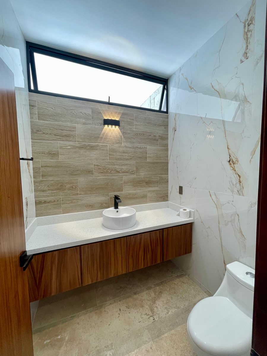 Medio baño de visitas con lavabo de madera y muro tipo mármol en casa en venta en Mazatlán