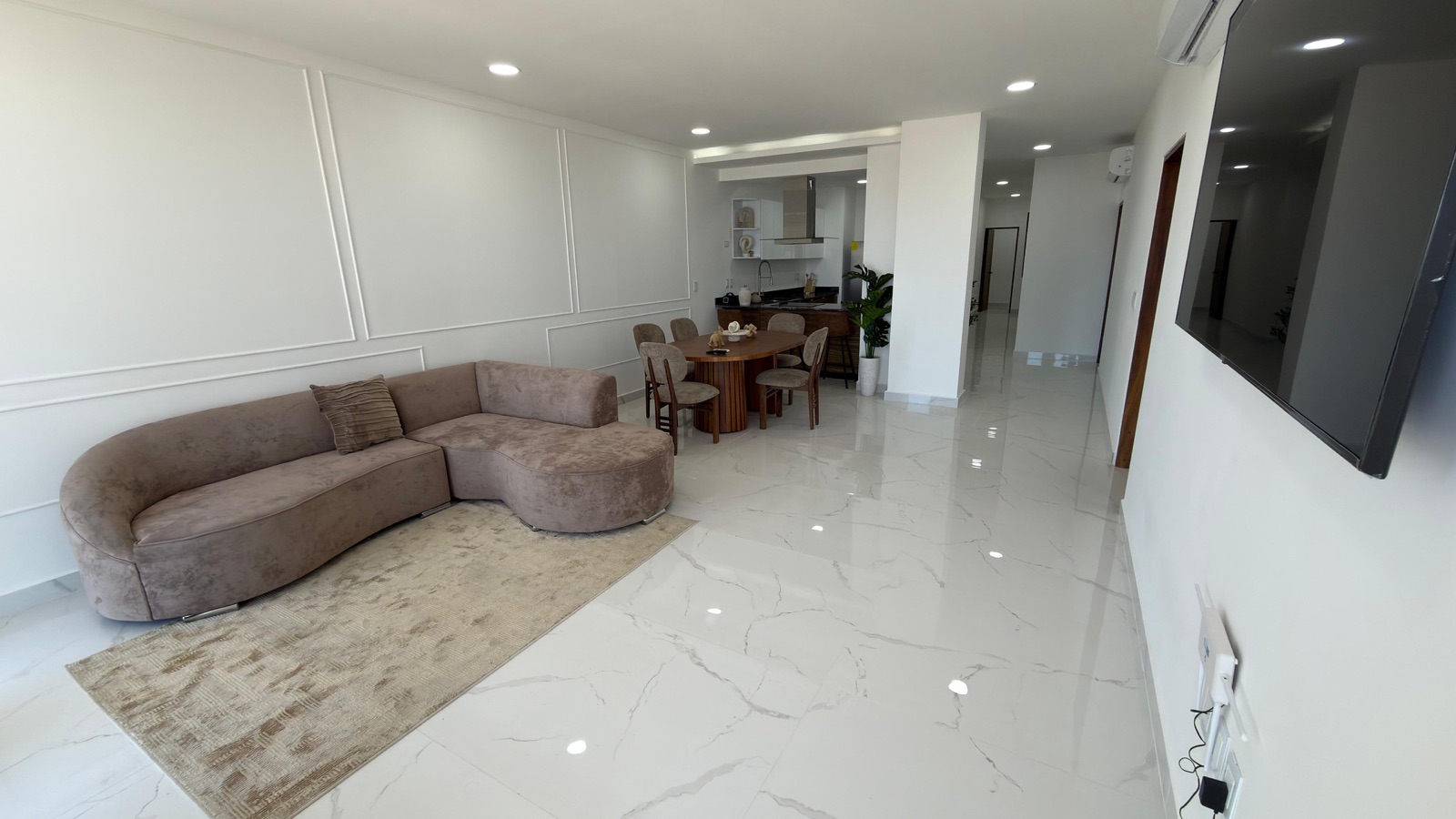 Amplia sala con sofá curvo y comedor junto a ventanales con vista al mar en Mazatlán