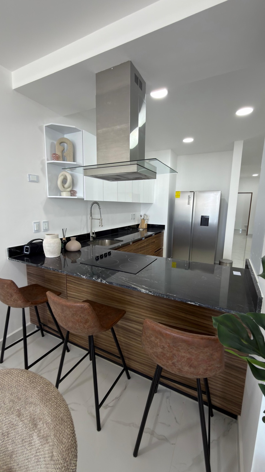 Cocina integral con isla de granito negro, campana de acero y desayunador en departamento en Mazatlán
