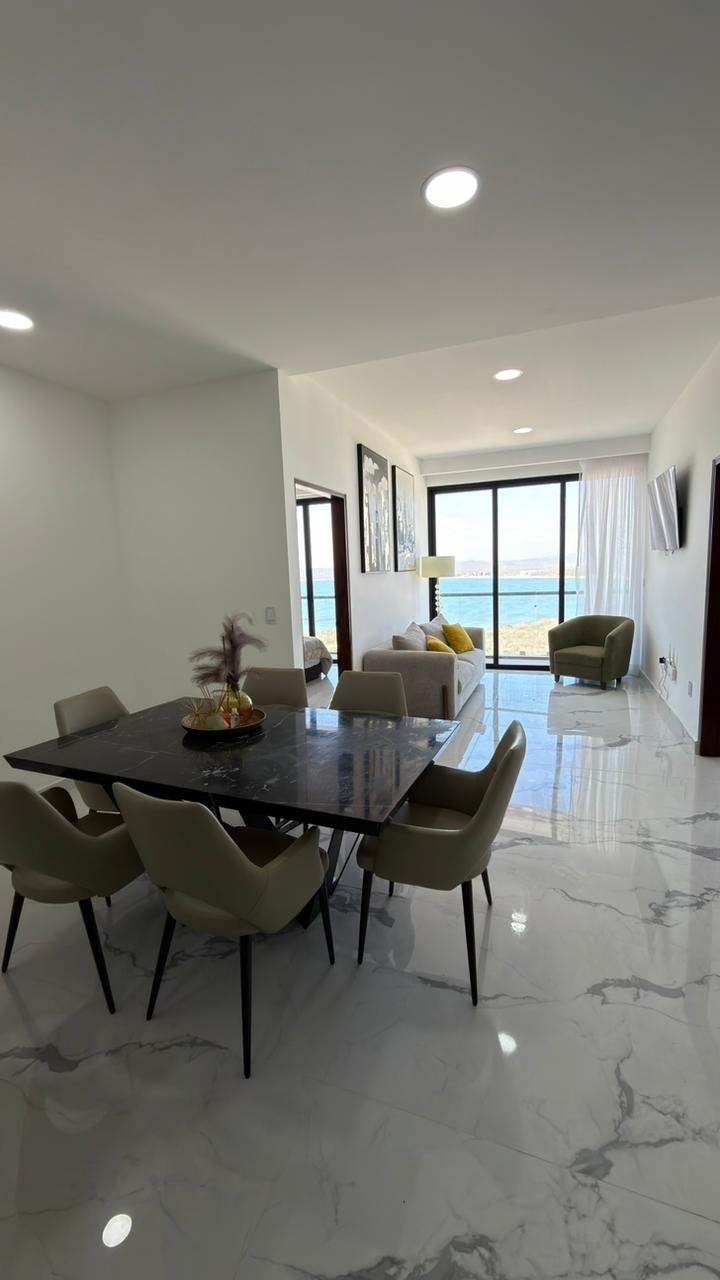 Sala y comedor amueblados con ventanal y vista a la bahía en departamento frente al mar en Mazatlán